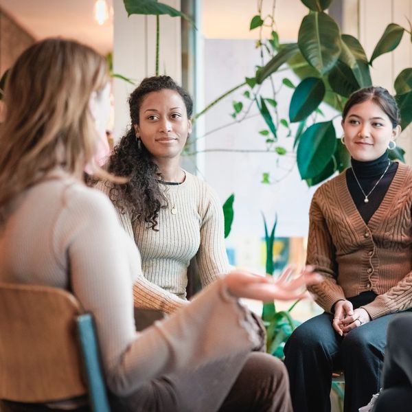 A group of four women engaged in a thoughtful conversation indoors.