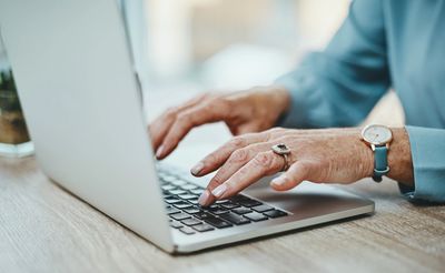 Close-up of elderly hands typing on a laptop keyboard virtually attending professional development.