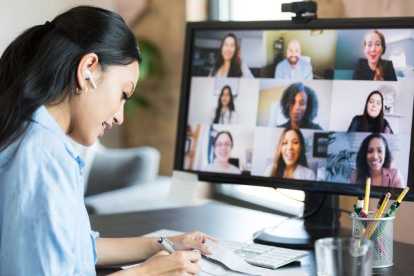 Woman participating in a virtual meeting and taking notes.