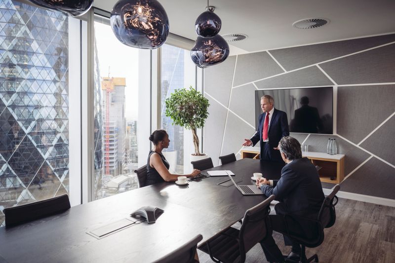 Diverse group of businesspeople in 30s, 40s, and 50s sitting at conference table with floor-to-ceiling view and exchanging ideas for financial strategies.