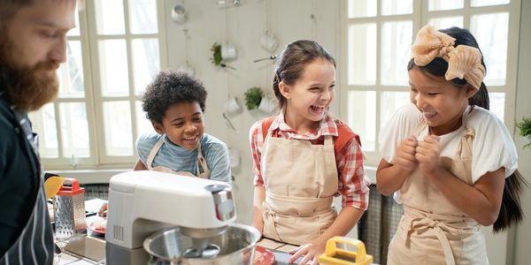 Three children wearing aprons happily baking together.