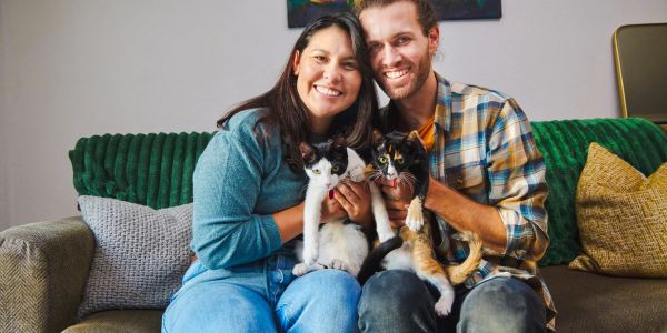 A happy couple holding two cats on a couch.