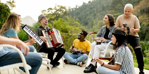 Group of friends joyfully playing various musical instruments outdoors.