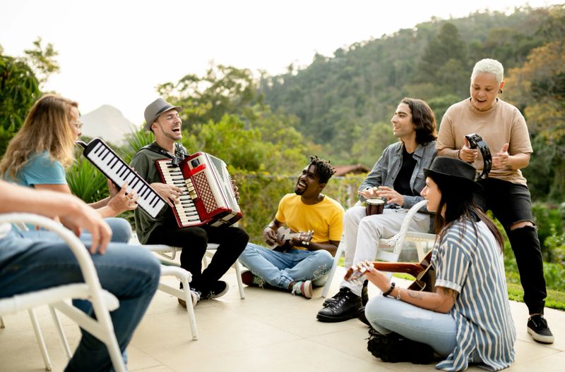 Diverse group of smiling young band members jamming together outside with a variety of eclectic musical instruments