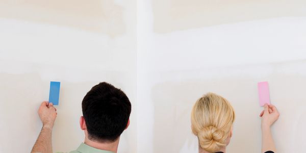 Couple holding paint color samples against a wall for comparison.