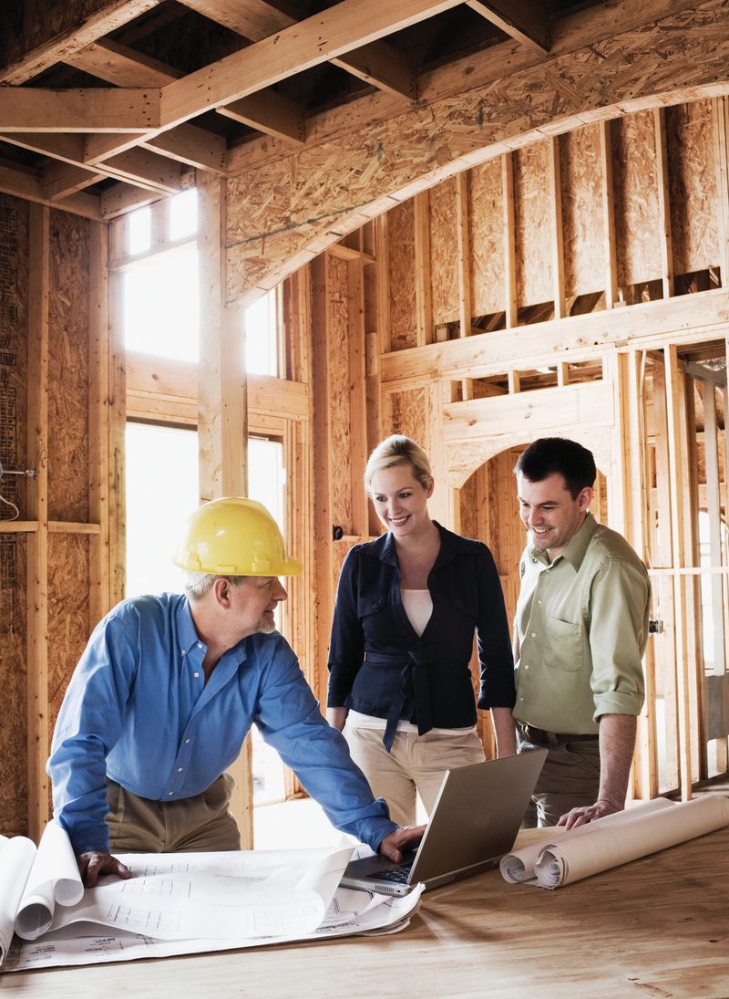 A young couple is meeting with their homebuilder at the construction site looking over blueprints.