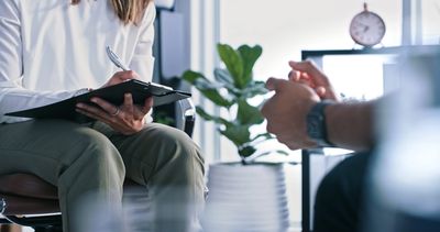 A therapist taking notes while listening to a patient in a calm office setting.
