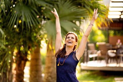 Joyful woman raising her arms outdoors in a sunny garden.