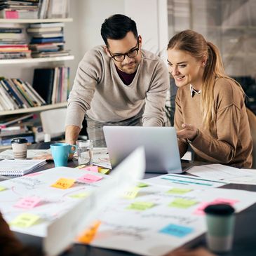 Two creative professionals collaborating with laptop and posters with sticky notes on table.