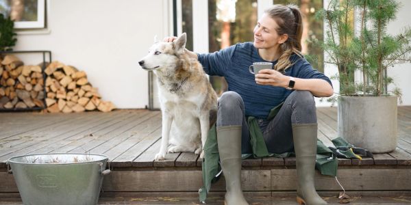 Woman sitting on porch with her dog, holding a cup.