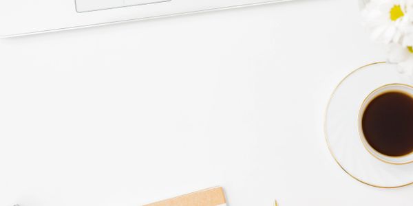 A stylish workspace with a laptop, striped notebook, gold pen, and coffee cup.