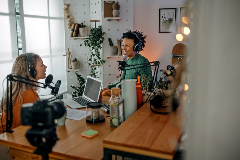 Smiling young women recording podcast and interview with female guest using microphone and headphone in recording studio