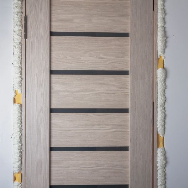 A modern wooden door with horizontal black stripes and expanding foam insulation around the frame.