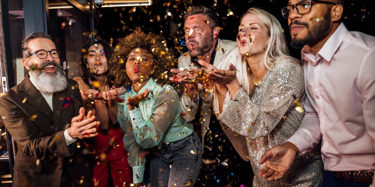 A diverse group joyfully blowing confetti at a celebration party.
