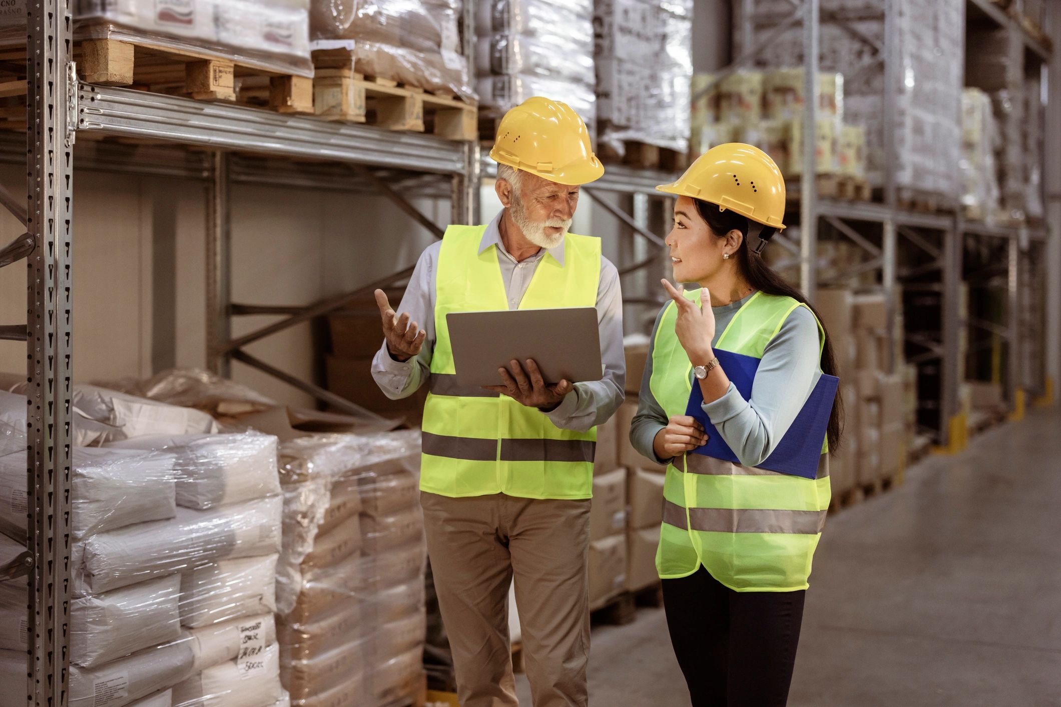 Supervisor and new worker in safety vests and hard hats reviewing a checklist in a warehouse