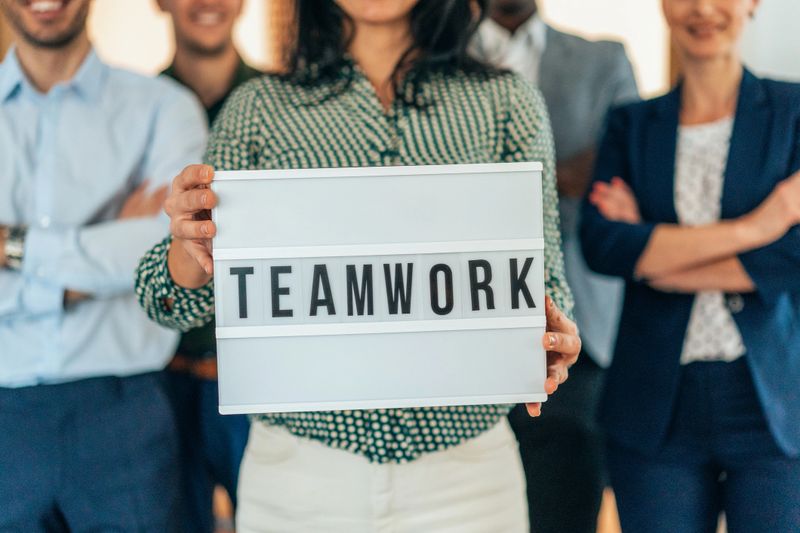 Portrait of multi ethnic successful business team looking at camera in the office and team leader holding  sign ''teamwork'' in hands