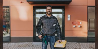 A man holding tools and a yellow toolbox outside a building.