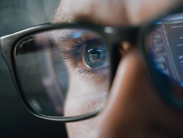 Close-up of a person wearing glasses reflecting computer code on the screen.