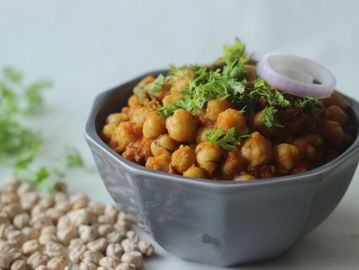 A bowl of spicy chickpea curry garnished with fresh cilantro and onion.