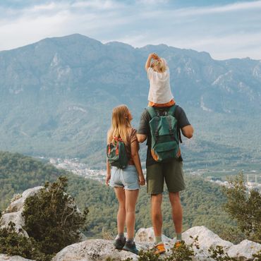 Family hiking with child on shoulders overlooking mountain landscape.