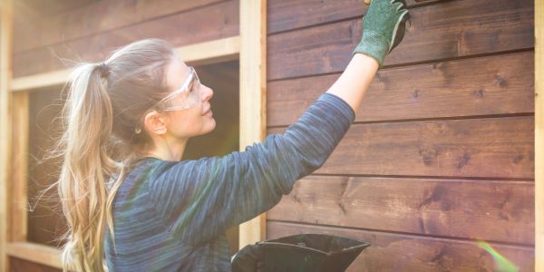 Une femme peint une maison en bois.