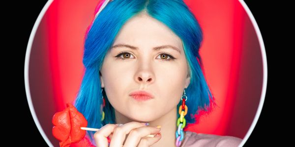 Young woman with blue hair holding a red rose lollipop.