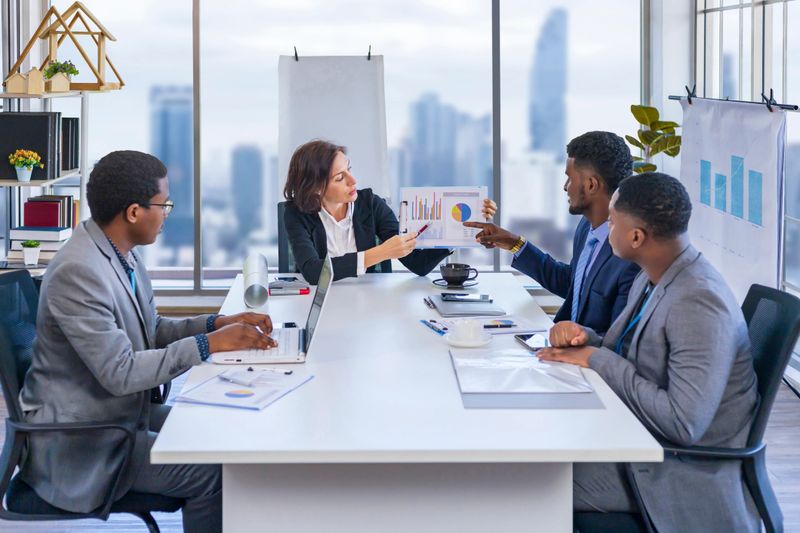 Woman manager is showing annual report chart to her African American colleagues in the executive meeting for next year plan with city skyline background for global business and investment
