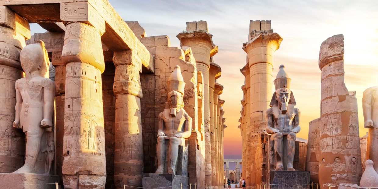 Ancient Egyptian temple with towering statues and columns at sunset.