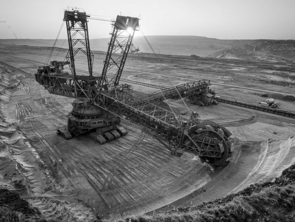 A massive mining excavator working in an open-pit mine during sunset.