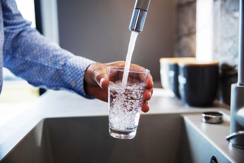 Mature male hand  pouring a glass of water from tap in the kitchen sink