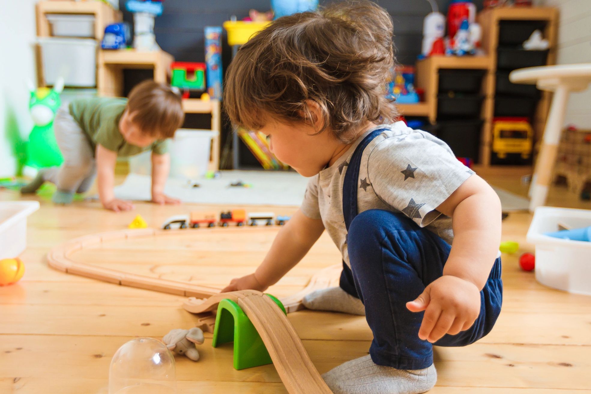 Two children playing with a wooden train set indoors.