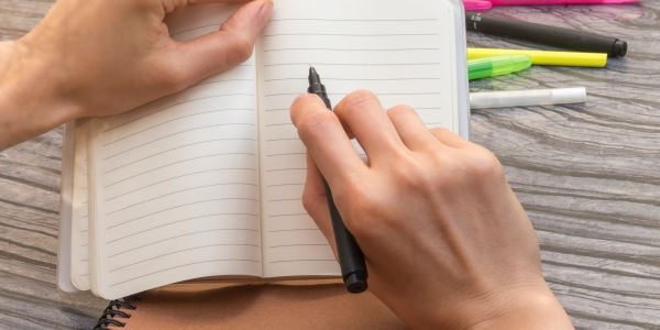 Person holding a pen over a blank notebook page.