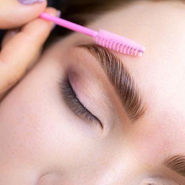 Close-up of eyebrow grooming with a pink brush.