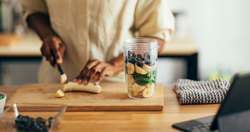 Unrecognizable African American woman making healthy breakfast while using digital tablet on a kitchen table.