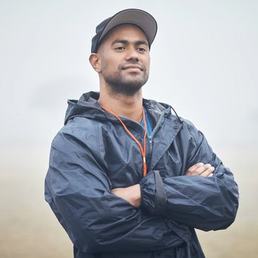Confident man in a rain jacket and cap with arms crossed.