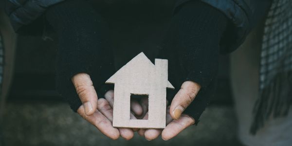Hands in gloves holding a small cardboard house model.