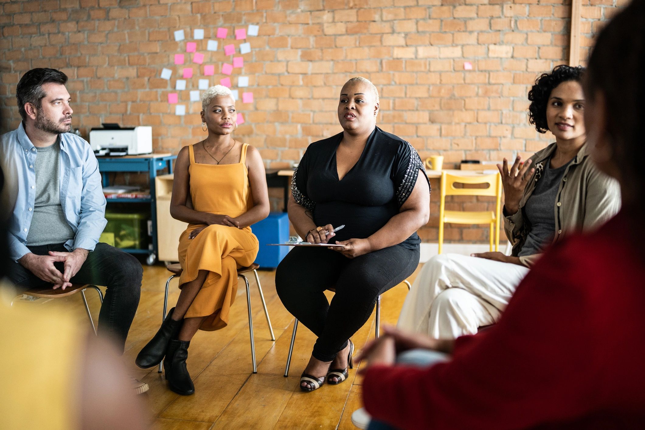 Diverse group engaged in a serious discussion in a cozy room with sticky notes on the wall.