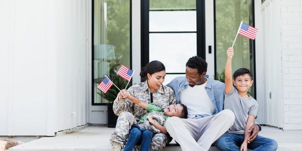 Photo of a mixed military family of 4. Mom is the service member holding American flags