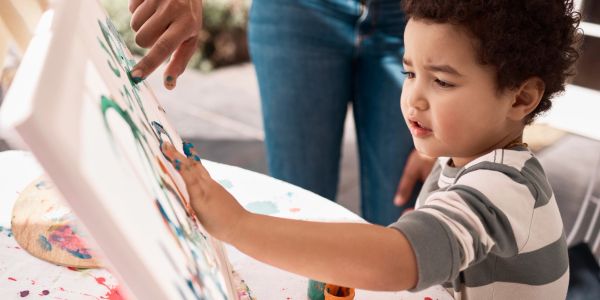 Child painting on canvas with adult guidance.