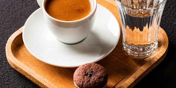 Cup of coffee with a glass of water and a chocolate muffin on a wooden tray.