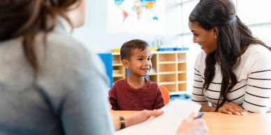 A young boy smiles during a conversation with a woman at a table.
