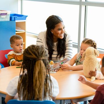 Teacher engaging with diverse young children in a classroom around a table.