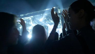 People enjoying a concert with hands raised in a dark venue.