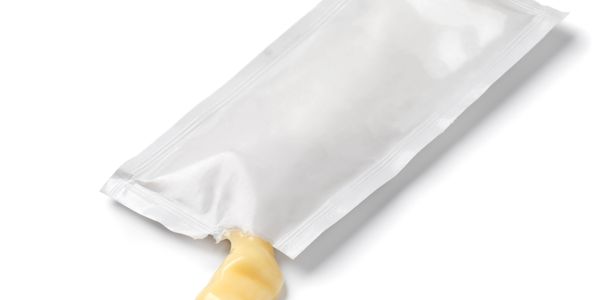 Squeeze packet with yellow sauce spilling out on white background.