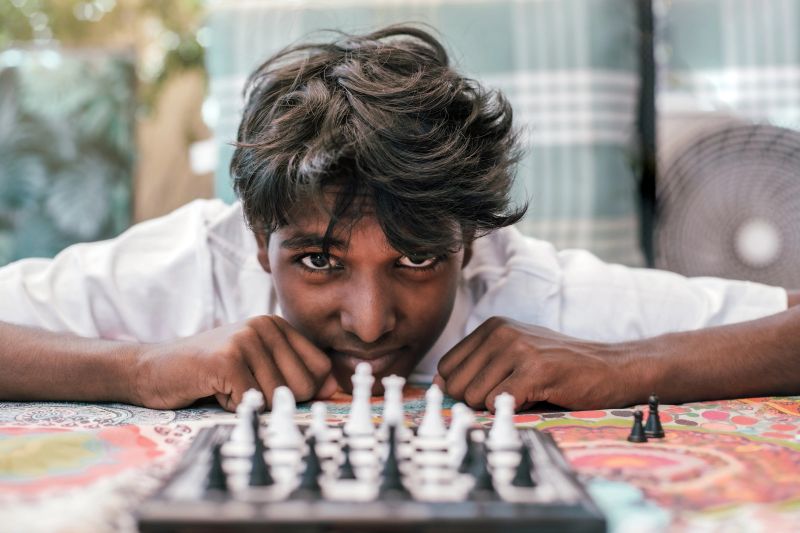 a boy of Indian origin, stares at the camera while playing chess. Front view. Portrait of an Indian boy with a chess board.