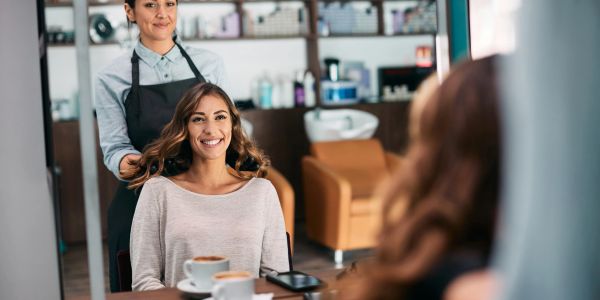 Woman smiling at salon mirror with hairstylist behind her.