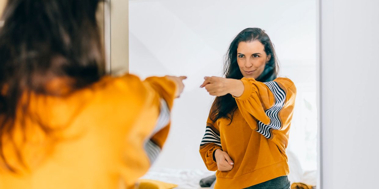 Woman looking in mirror being compassionate to herself.
