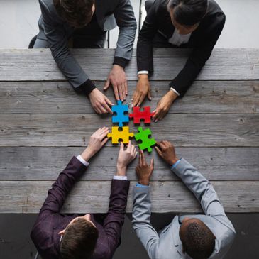 Four professionals connecting colorful puzzle pieces at a wooden table.