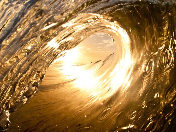 Golden sunlight shining through a curling ocean wave at sunset.