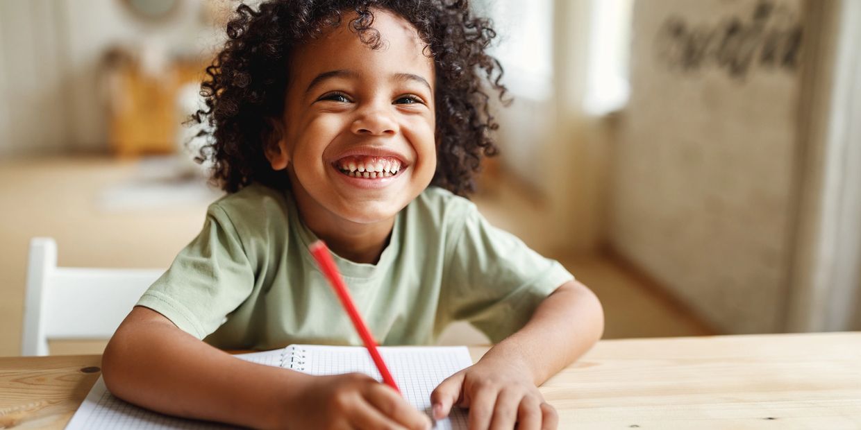 Happy child smiling while drawing with a red pencil.